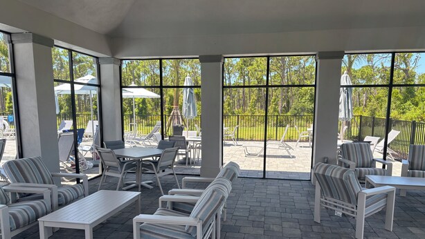 Un'area patio coperta con posti a sedere all'aperto, tra cui tavoli e sedie, e ampie finestre che offrono viste sul verde circostante.
