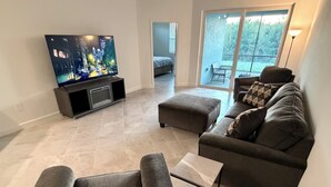 Un soggiorno moderno con una TV a schermo piatto, un divano grigio, un tavolino da caffè e una porta vetrata scorrevole che dà su un balcone.