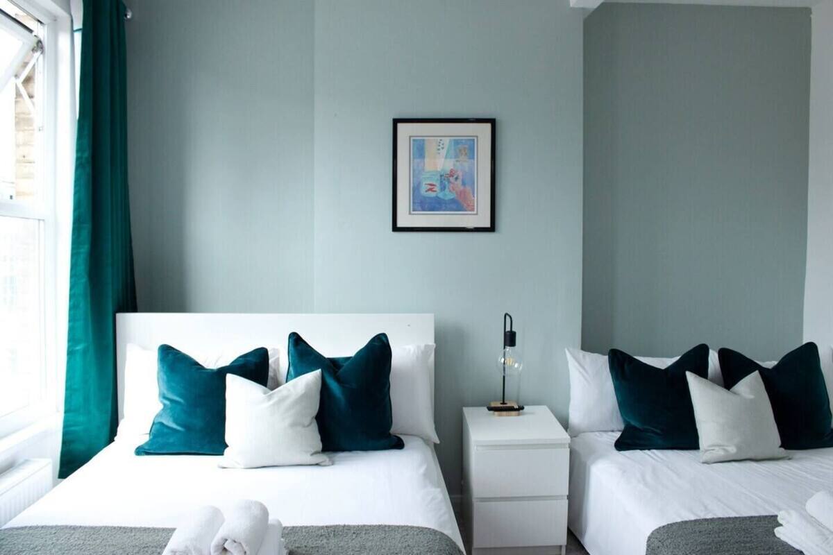 A hotel room with two beds, a nightstand with a lamp, a framed picture on the wall, and a window with curtains.
