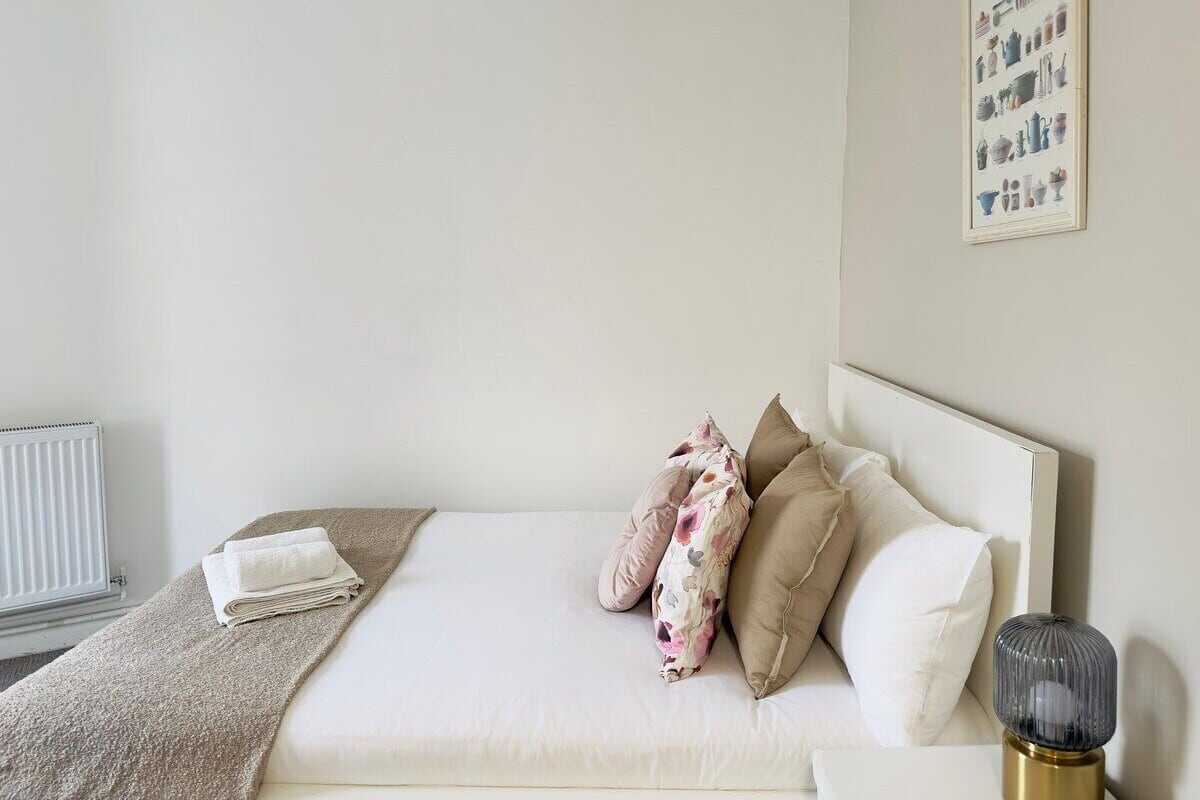 A neatly made bed with a white comforter, beige pillows, and a floral throw blanket.