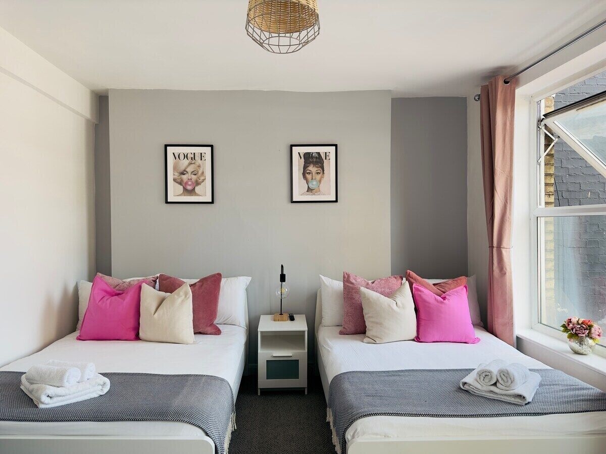 Une chambre d’hôtel avec deux lits, une table de chevet, une lampe et une fenêtre avec des rideaux.