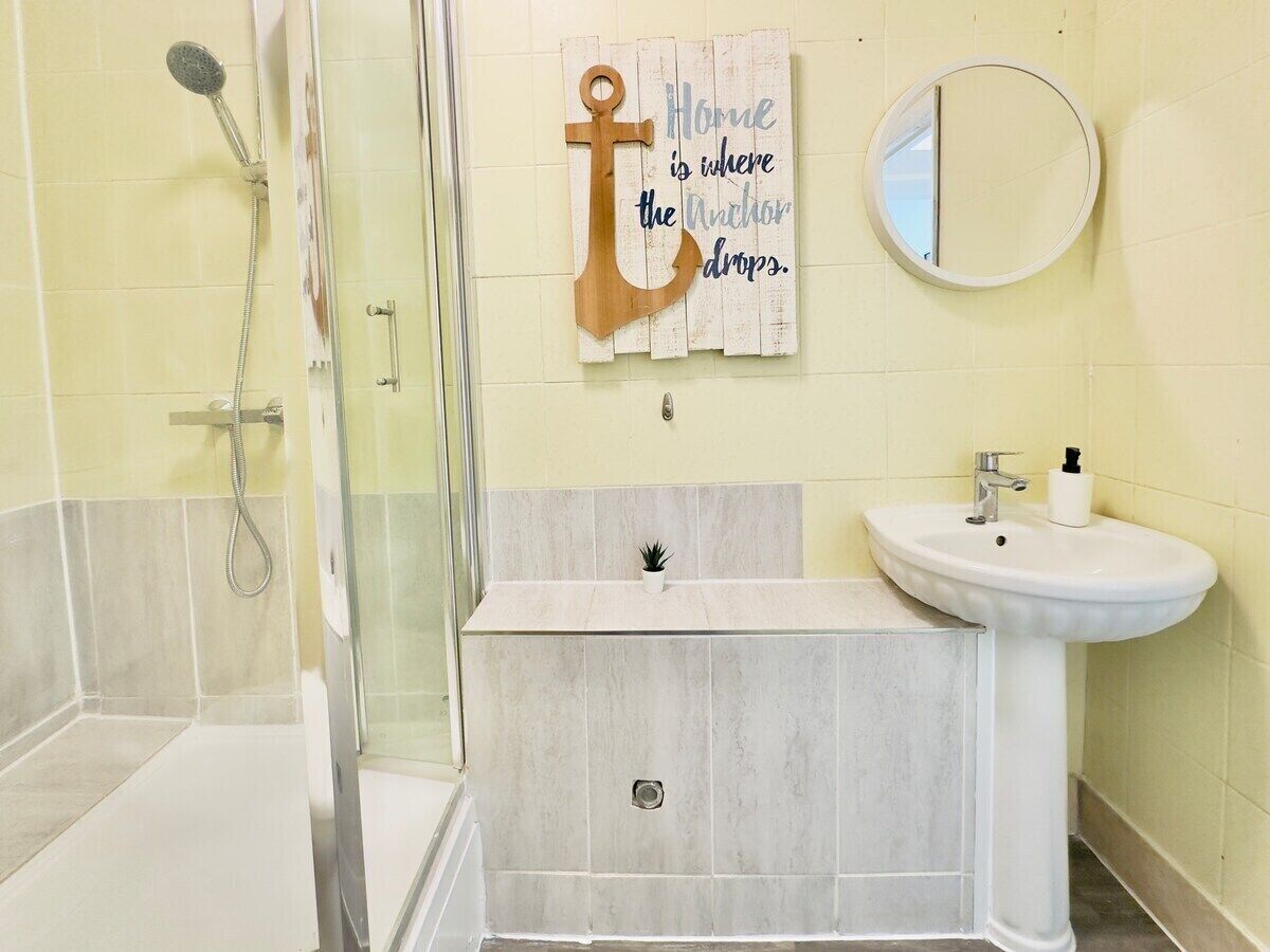 A bathroom with a shower, a sink, a mirror, and a decorative anchor sign.