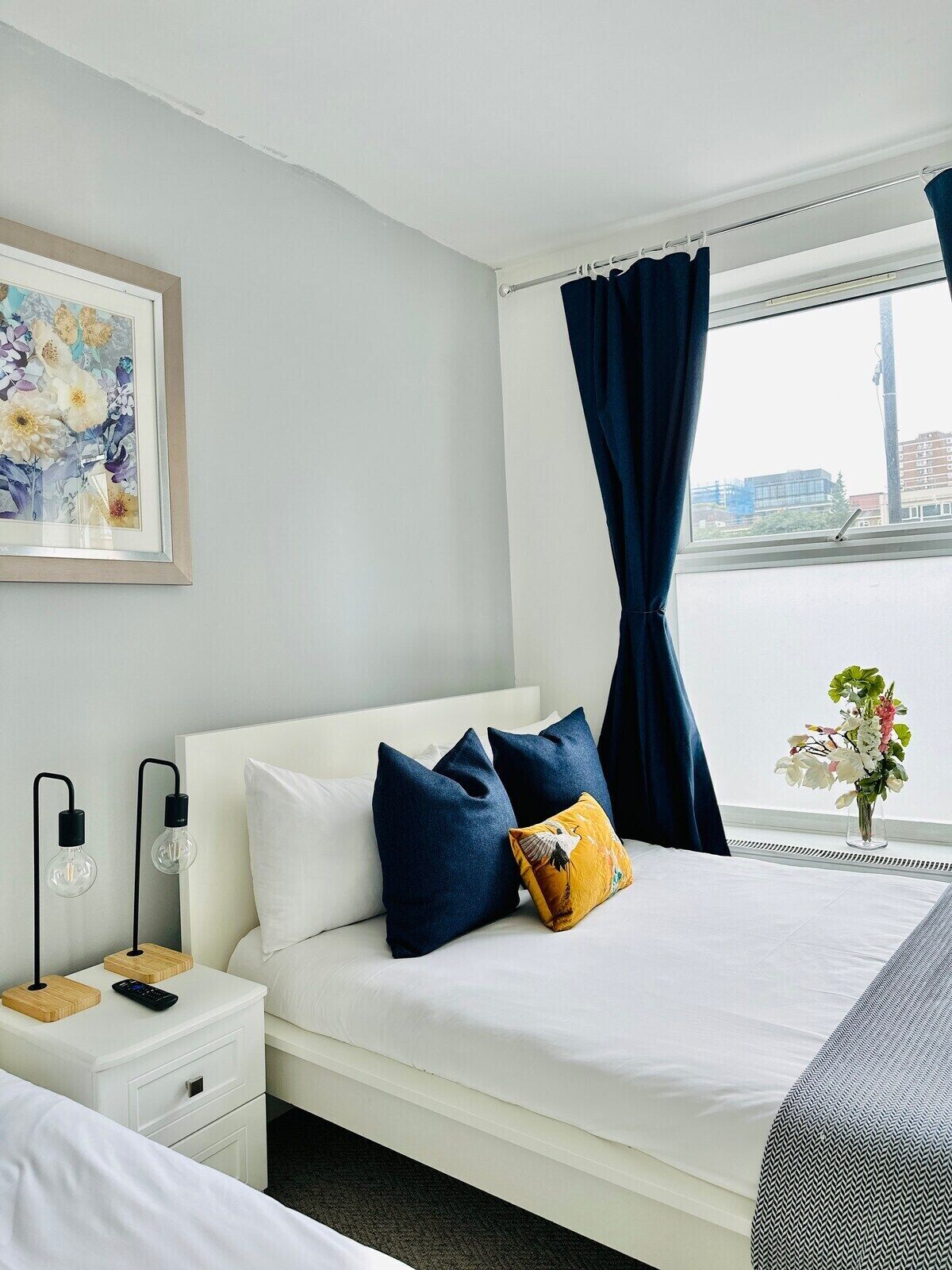 Une chambre d’hôtel avec un lit, une table de chevet, une lampe et une vue sur un immeuble par la fenêtre.