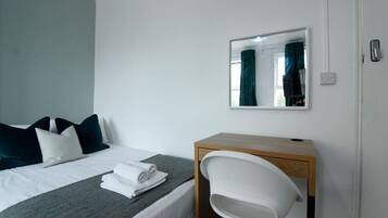 A hotel room with a bed, a desk, a chair, a mirror, and a window with curtains.