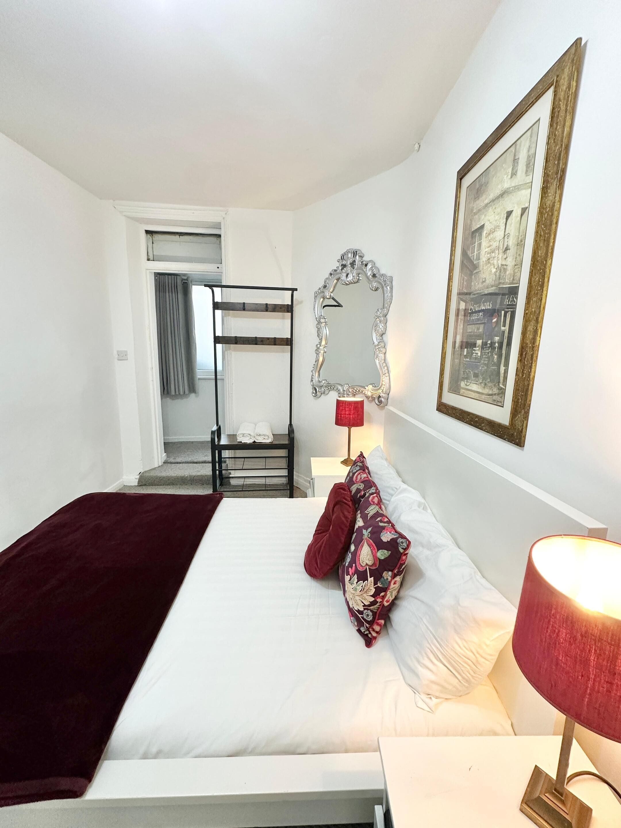 A hotel room with a bed, a red lamp, a mirror, and a framed picture on the wall.