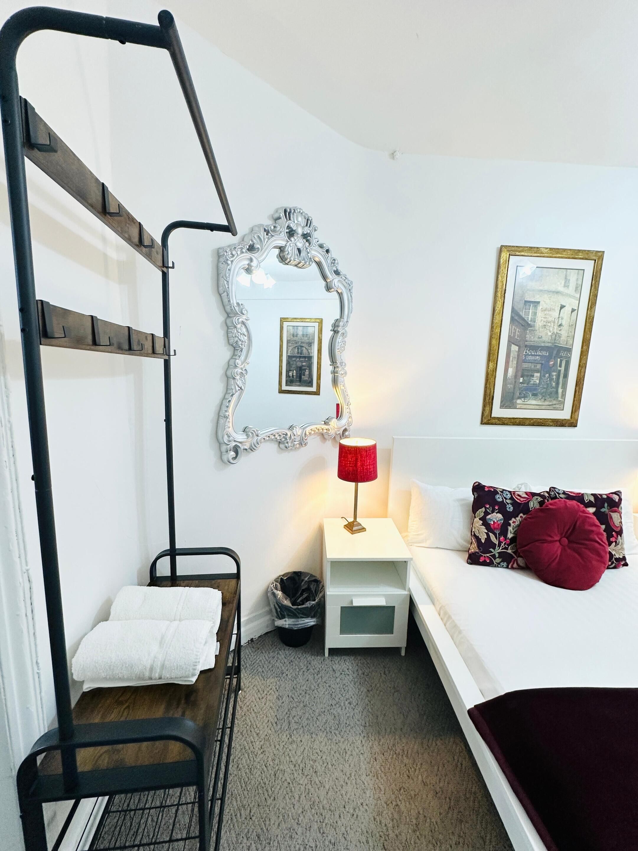 A bunk bed with a white headboard, a small bedside table with a red lamp, a framed picture on the wall, and a bed with a floral pillow.