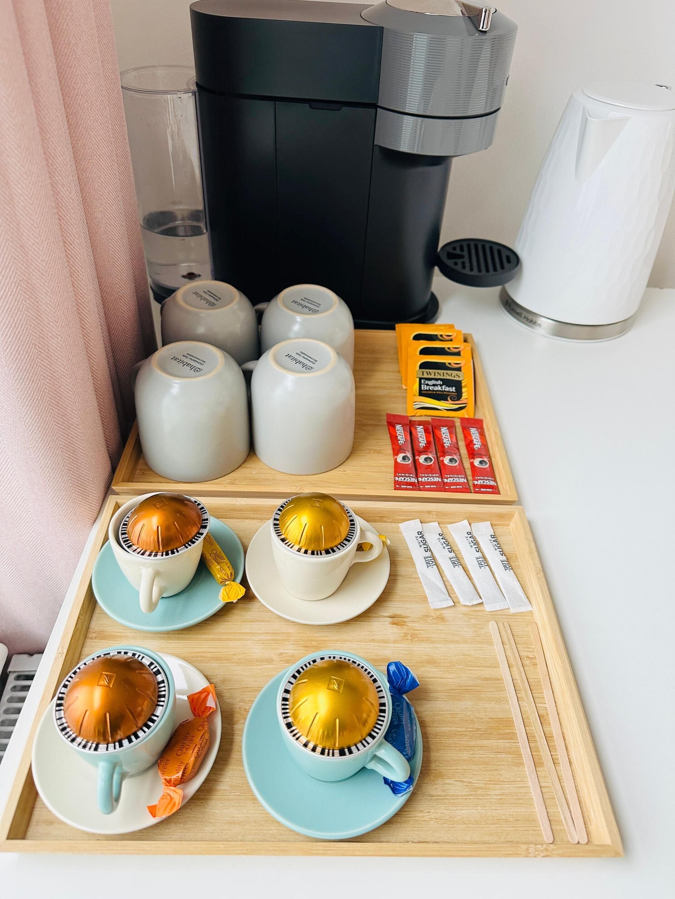 A tray with coffee cups, a coffee maker, and breakfast items.