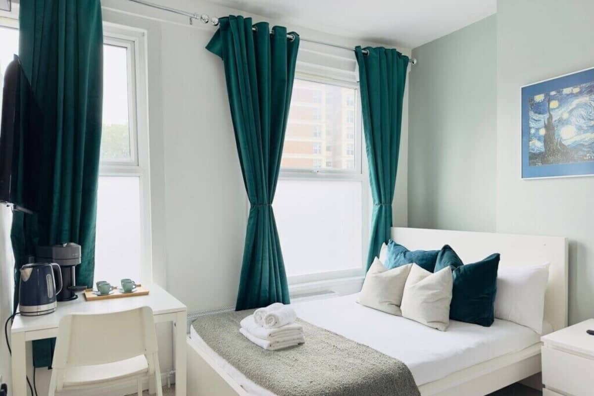 A hotel room with a bed, a desk, a chair, and a window with curtains.