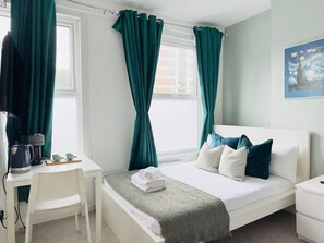 Une chambre d’hôtel avec un lit, un bureau, une chaise et une fenêtre avec des rideaux.