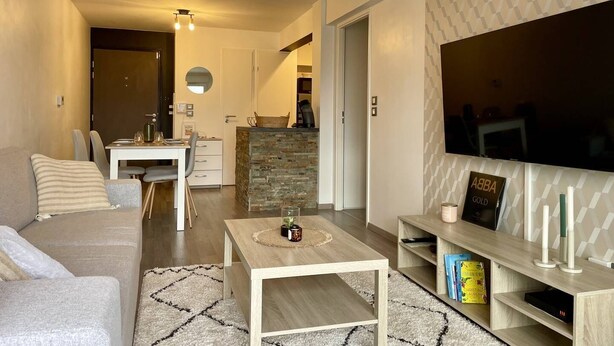 A modern living room with a sofa, a coffee table, and a TV on a wall. There is a kitchen area in the background. - Proche du centre et plage, confort garanti (LA ROCHELLE)