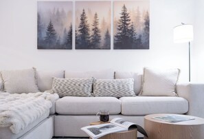A modern living room with a light grey sofa, a white throw blanket, a coffee cup, and a magazine on a wooden side table. - Luxury Condo with Private Hot Tub (Revelstoke)