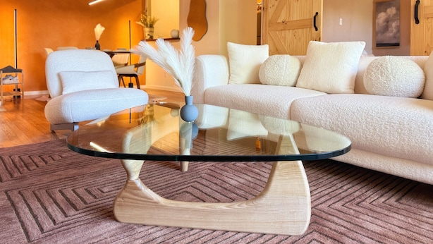 Ein modernes Wohnzimmer mit einem Glastisch, weißen Sofas mit Strukturmuster und Holzboden.