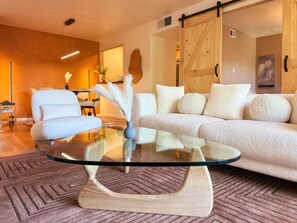 Un salon moderne avec une table basse en verre, des canapés blancs à texture intéressante et un plancher en bois.