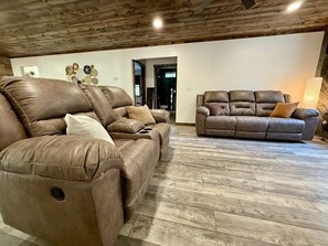 Un amplio salón con dos sofás de cuero, techo de madera y un suelo con diseño de espiga.