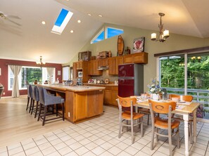 A spacious kitchen with a central island, wooden cabinets, and a large window offering a view of the outdoors. - Siuslaw River House *Casino*River*Beach*Pets*Pool (Florence)