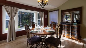 Comedor con una mesa redonda dispuesta para cuatro personas, rodeada de sillas, una araña y un mueble de madera con cajones.