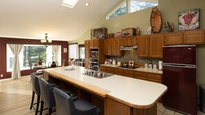 Una cocina amplia con armarios de madera, una isla grande con taburetes de bar, un refrigerador y un ventanal que proporciona luz natural.