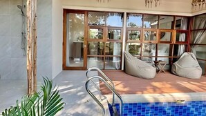 A modern pool area with a glass door leading to a dining area, a wooden deck, and a metal ladder. - Villa Uluwatu - Belle Vue Jungle, Villa 23 (Koh Samui)