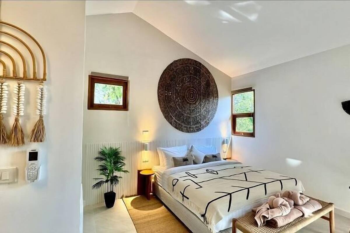Een moderne slaapkamer met een bed, bedlampen, een groot kunstwerk aan de muur en een klein raam.