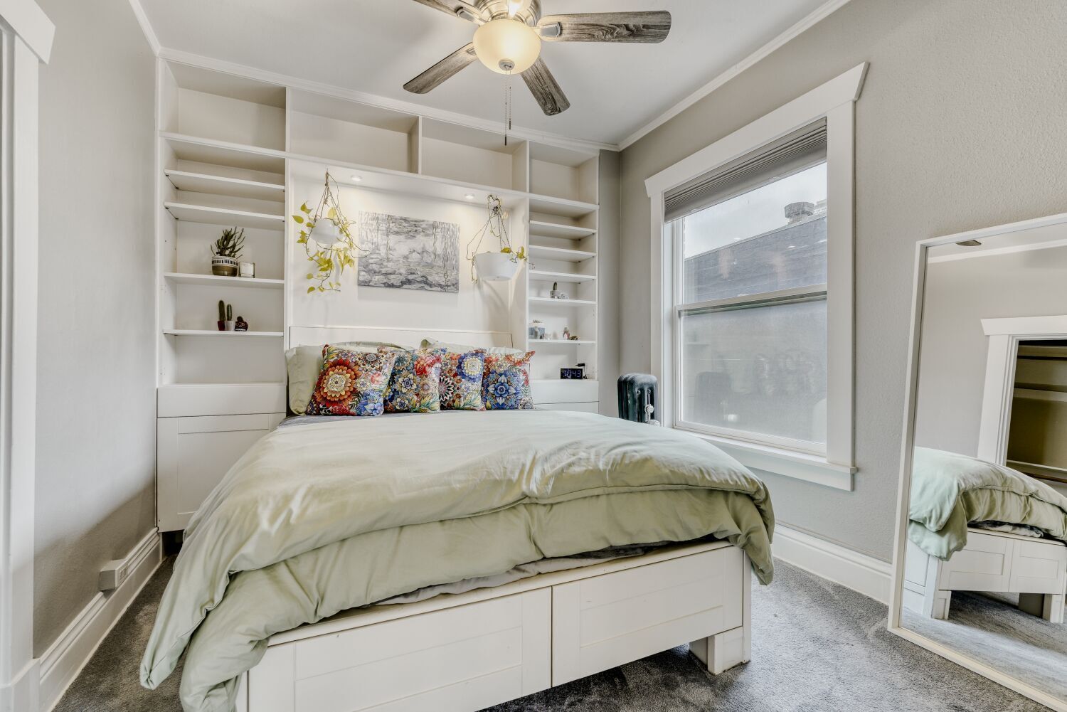 Un dormitorio con cama, estanterías empotradas, ventilador de techo y un amplio ventanal.