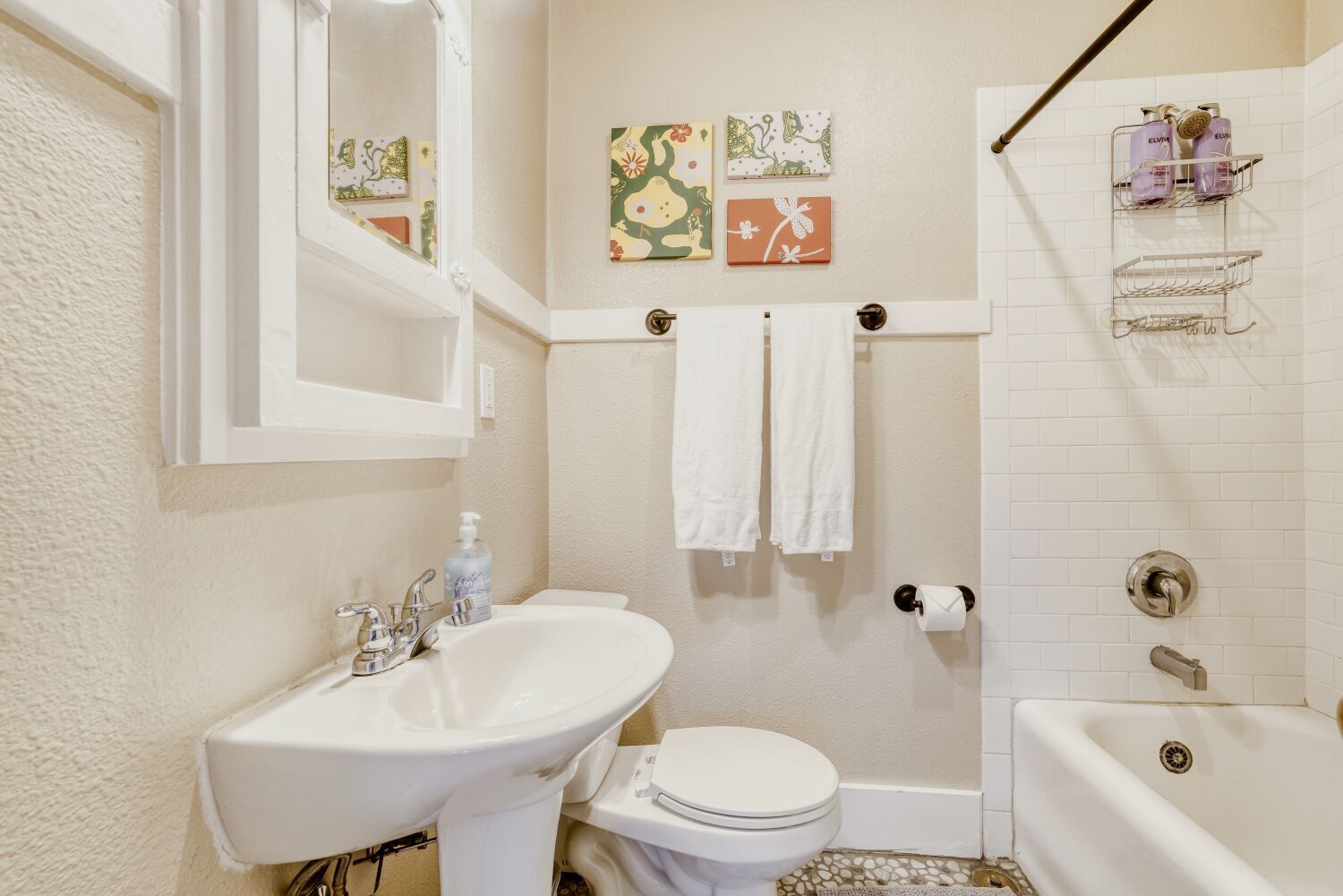 A bathroom with a sink, toilet, bathtub, and shower. There are towels hanging on a rack and artwork on the wall.