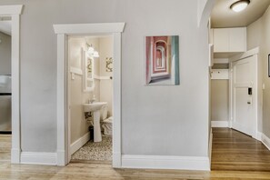 Un couloir avec un sol carrelé, une porte blanche et un tableau accroché au mur.
