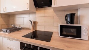 A kitchen with a black induction cooktop, a microwave, a kettle, and a sink with a utensil holder.