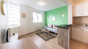 A modern apartment with a green accent wall, a sofa, a dining area, and a kitchen.