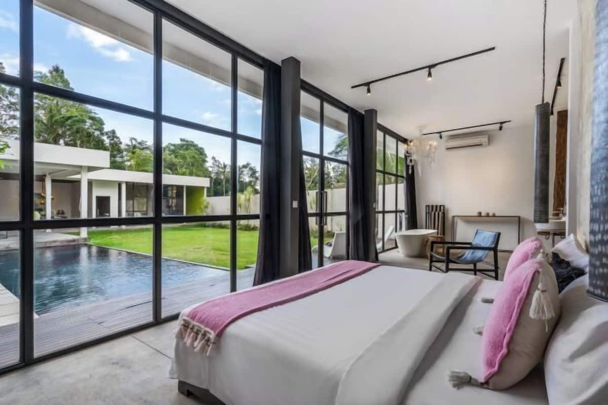 A modern bedroom with a large window, a bed, and a view of a swimming pool and outdoor area.