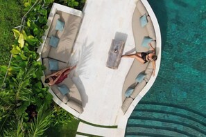 An aerial view of a poolside area with a lounge chair and a table, surrounded by greenery. - Villa Crystal Lagoon by BaliSuperHost (Bali)