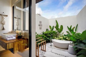 A modern bathroom with a freestanding bathtub, a wooden vanity, and a large window overlooking a garden. - Villa Crystal Lagoon by BaliSuperHost (Bali)