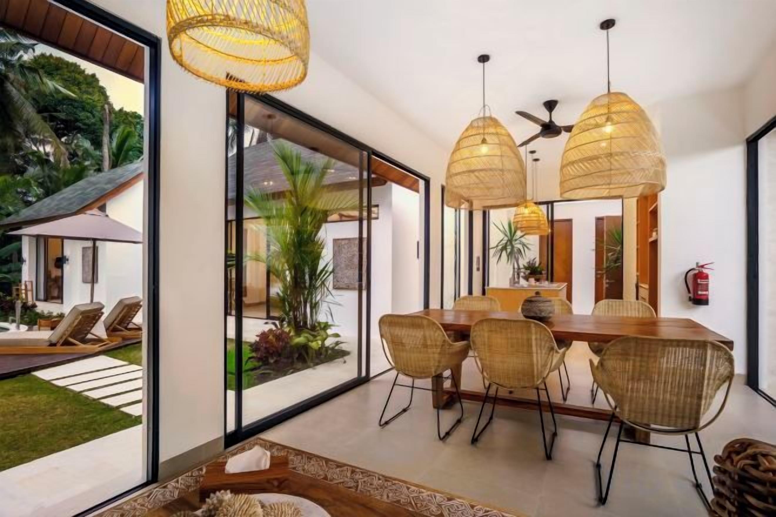 A dining area with a large table, wicker chairs, and hanging light fixtures.
