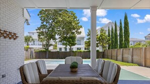 Un porxo cobert amb piscina, mobles de vimet i vista a una zona residencial.