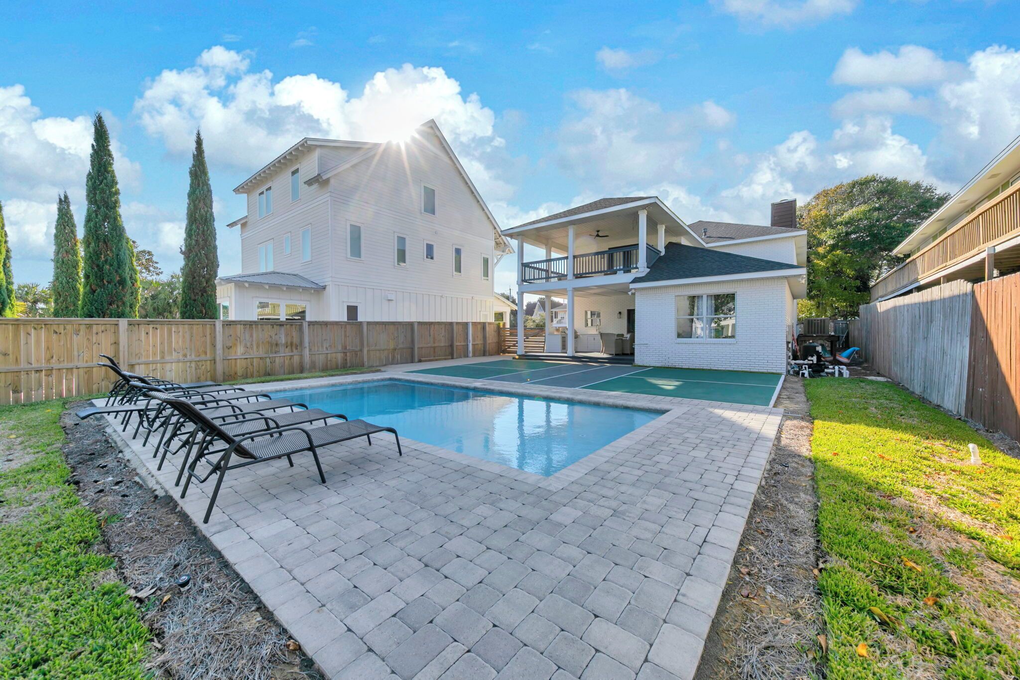 A swimming pool with lounge chairs, a wooden fence, and a two-story house with a balcony.