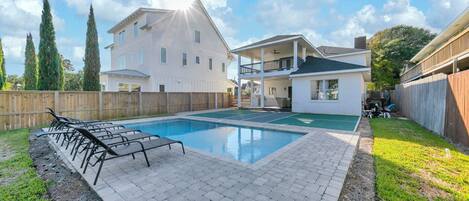 A swimming pool with lounge chairs, a wooden fence, and a two-story house with a balcony.