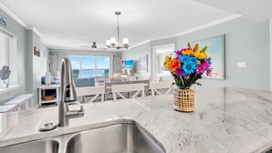 Uma cozinha moderna com bancada de mármore, pia de aço inoxidável e um vaso com flores coloridas.