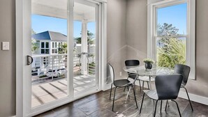 A modern room with a glass table and chairs, large sliding glass doors, and a view of a residential area. - 🦩Book Me Baby! Take Me Away in Miramar Beach 🦩 (Miramar Beach)
