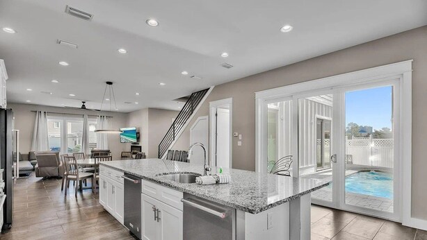A spacious kitchen with a granite countertop, a built-in dishwasher, and a large island. There is a dining area with a table and chairs, and a view of a swimming pool through large sliding glass doors. - 🦩Book Me Baby! Take Me Away in Miramar Beach 🦩 (Miramar Beach)
