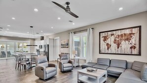 A spacious living room with a gray sofa, two armchairs, and a coffee table. There is a world map artwork on the wall and a ceiling fan. - 🦩Book Me Baby! Take Me Away in Miramar Beach 🦩 (Miramar Beach)