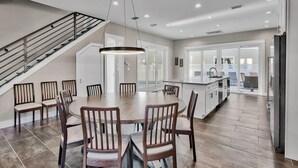 A spacious kitchen with a central island, a dining area with wooden chairs, and a staircase leading to an upper level. - 🦩Book Me Baby! Take Me Away in Miramar Beach 🦩 (Miramar Beach)