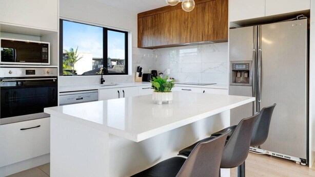A modern kitchen with a large island, stainless steel appliances, and a view of the city. - Modern Townhouse with Parking near Cornwall Park (Auckland South)