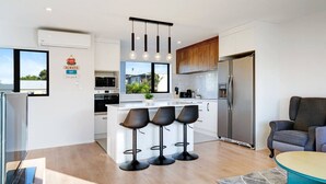 A modern kitchen with a central island, bar stools, a refrigerator, and a dining area with a table and chairs. - Modern Townhouse with Parking near Cornwall Park (Auckland South)
