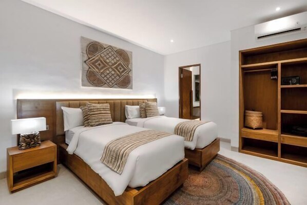 A modern bedroom with two beds, a wooden headboard, a bedside table with a lamp, a large mirror, and a wardrobe.