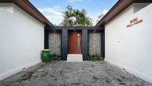 A modern building with a central entrance, two side walls, and a paved walkway leading to the door. - Villa Aman by BaliSuperHost (Bali)