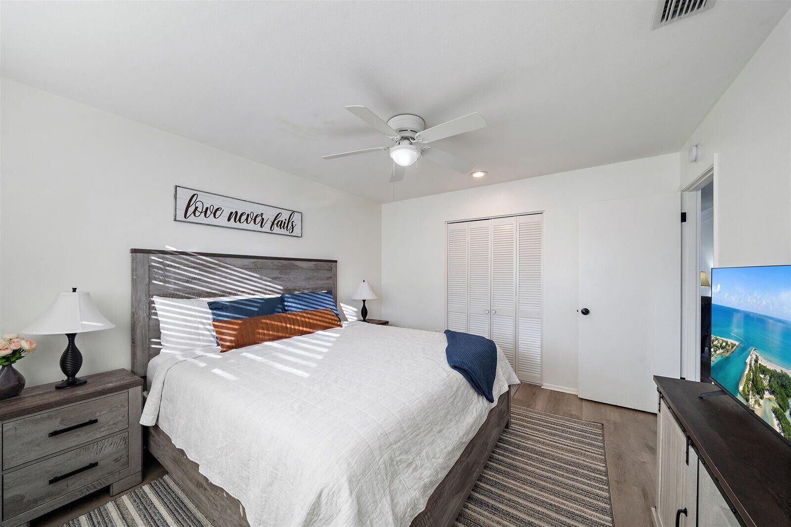 A bedroom with a bed, a ceiling fan, a wardrobe, a TV, and a motivational quote on the wall.
