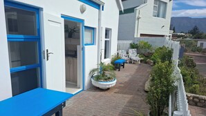Een woongebouw met een patio, voorzien van een blauwe tafel en stoelen, een witte hek en plantenbakken.