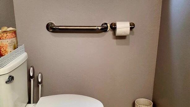 A bathroom with a toilet, a handrail, a window, and a trash can. - Silver Creek Accessible Studio (Helena)