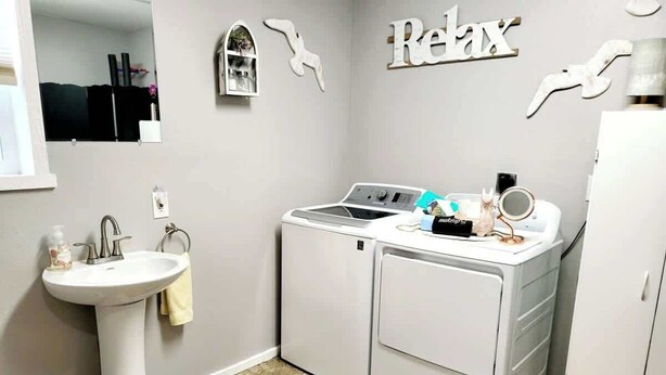 A compact laundry room with a washing machine, a sink, and a trash bin. - Silver Creek Accessible Studio (Helena)