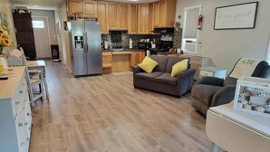 A modern kitchen with wooden cabinets, a stainless steel refrigerator, and a dining area with a table and chairs. - Silver Creek Accessible Studio (Helena)