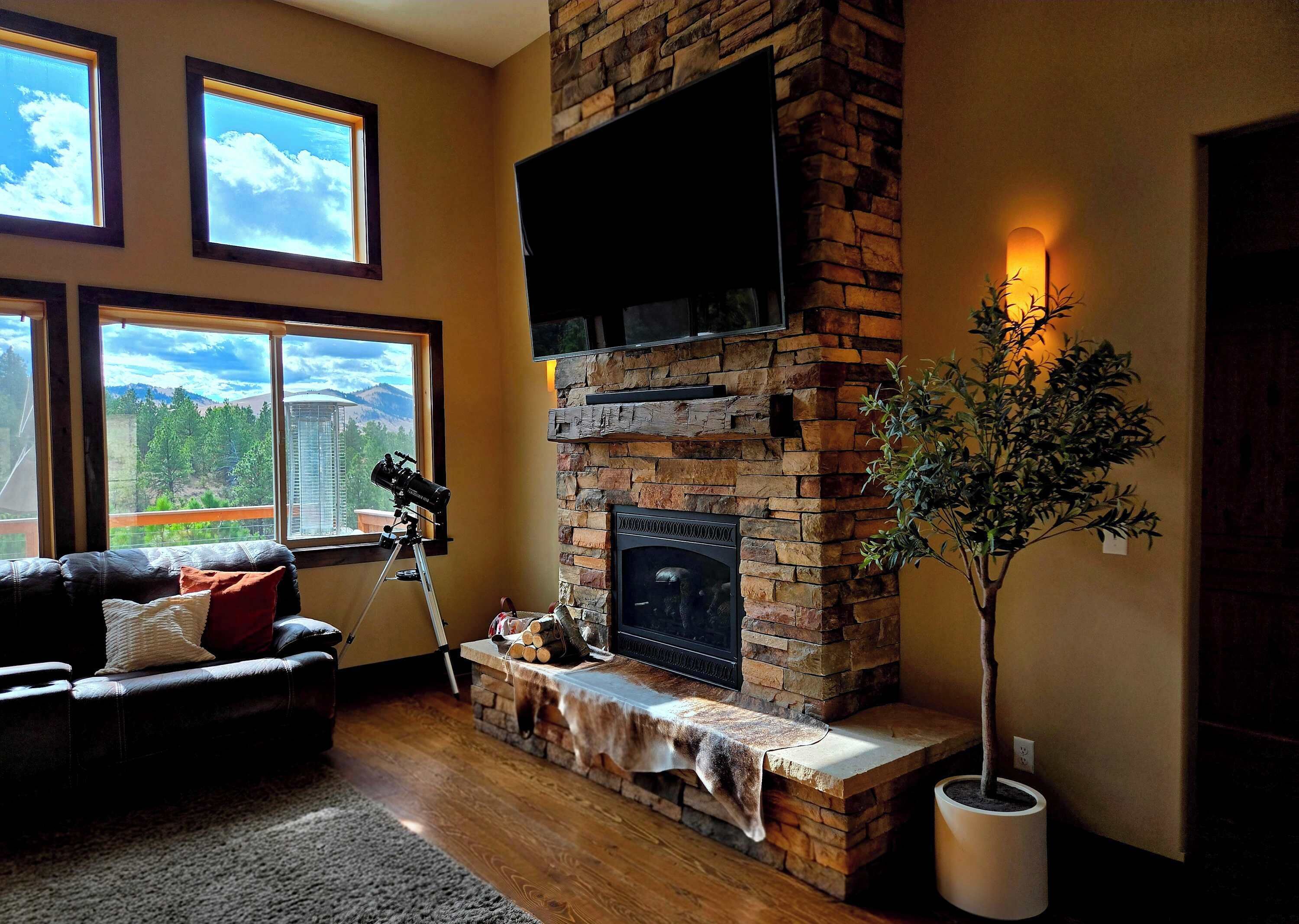 A living room with a fireplace, a telescope, and a large window with a mountain view.